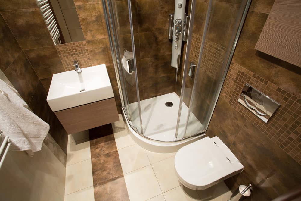 Small bathroom with brown tiles, corner shower, floating sink, and wall-mounted toilet.