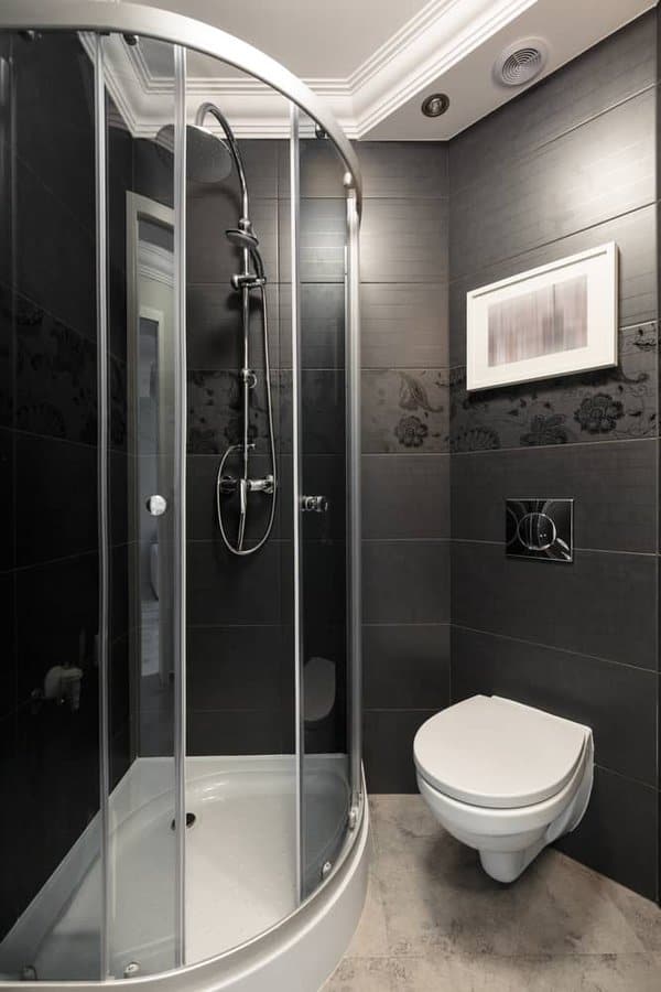 Compact bathroom with curved glass shower, black tiled walls, and wall-mounted toilet.