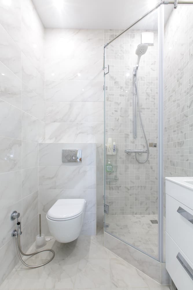 Bright bathroom with white marble tiles, glass shower, and wall-mounted toilet.