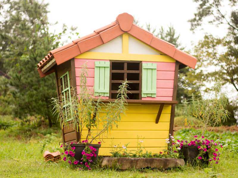 Colorful cottage-style garden shed with pastel shutters and potted flowers in a green yard.