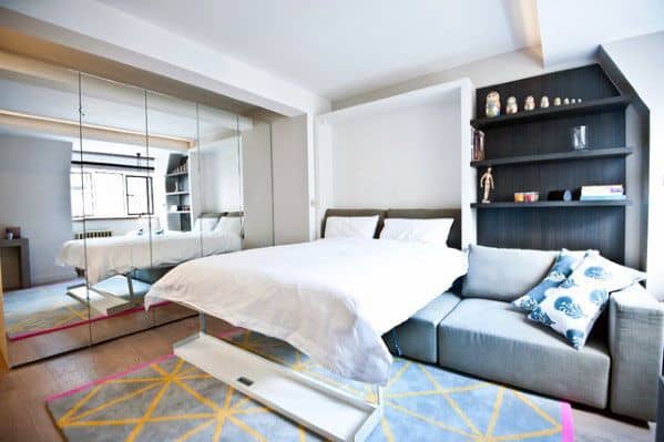 Studio apartment with a fold-out bed, mirrored closet, recessed shelves, and modern decor.