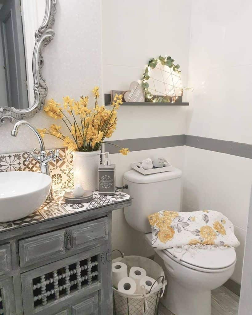 Cozy bathroom with floral decorations, basket of toilet paper, and a mirror above a sink with a decorative vase