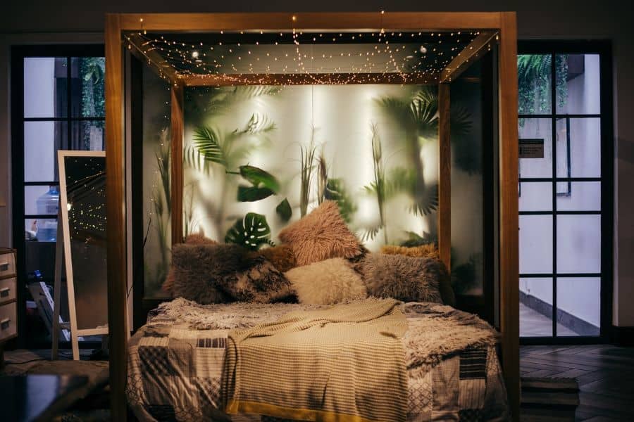 Lush boho canopy bed with fairy lights and tropical leaf decor, creating a dreamy retreat.