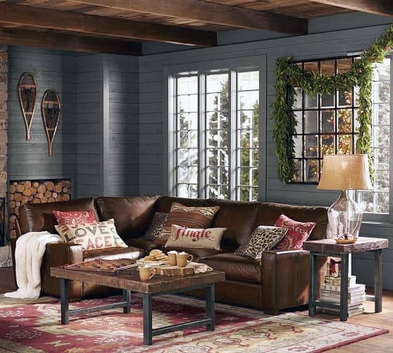 A cozy rustic living room with a leather sofa, festive pillows, a wooden coffee table, and warm, inviting decor, featuring a view of snowy outdoors