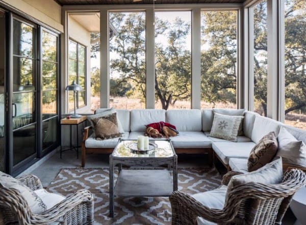 A cozy sunroom featuring a large sectional sofa, wicker chairs, and a patterned rug.