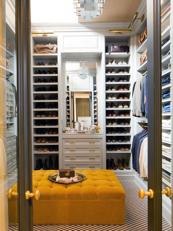 Luxurious walk-in closet with organized shoes, clothes on shelves, and a mustard ottoman in the center