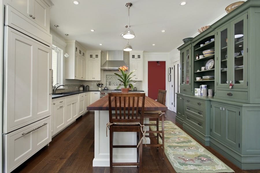 A modern kitchen with white cabinets, a green hutch, and a wood island crowned by a floral centerpiece