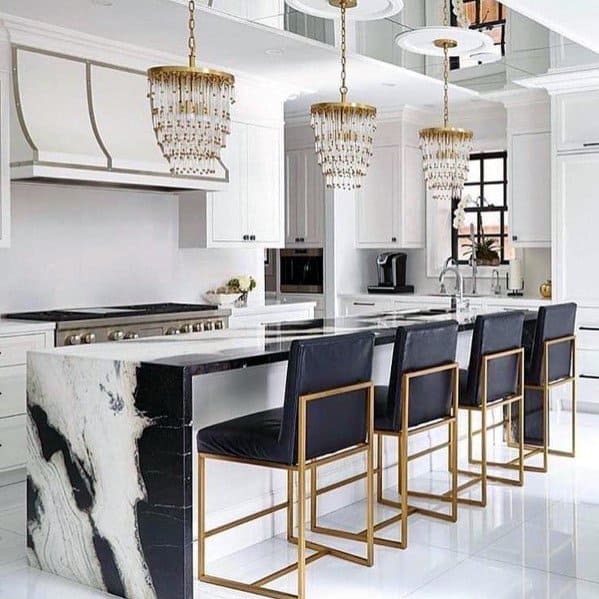 Elegant kitchen with crystal chandeliers above a black and white marble island, complemented by sleek gold-accented bar stools