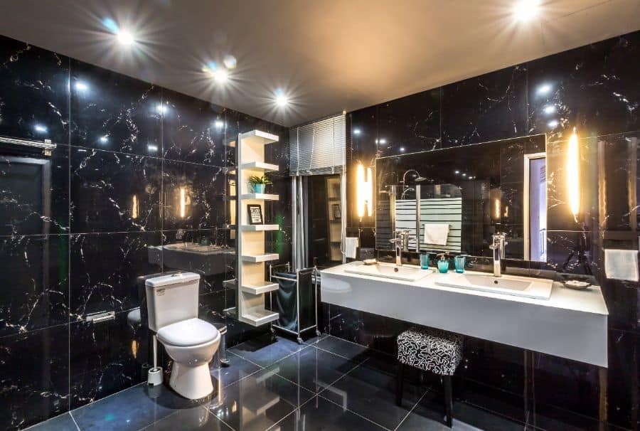 Luxurious bathroom with black marble tiles, double vanity, shelving, and modern lighting.