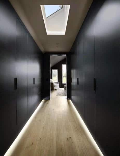 A sleek, modern hallway with dark walls, a wooden floor, and a skylight overhead