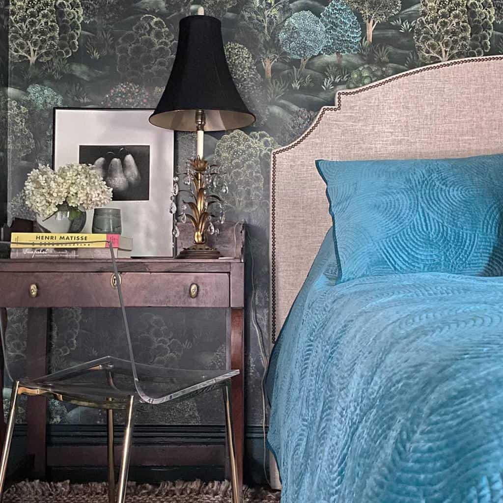 Bedroom with forest wallpaper, brown bedside table, black lamp, and blue bedding.