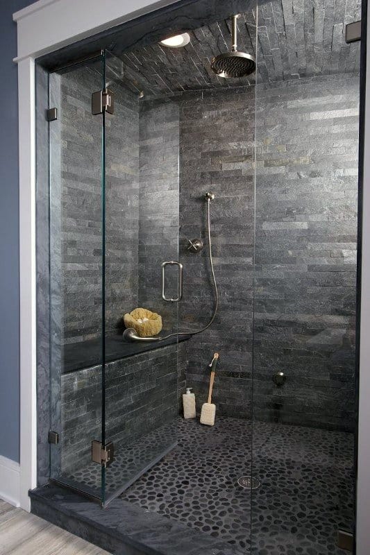 Gray natural stone shower with pebble floor, glass door, and built-in bench.