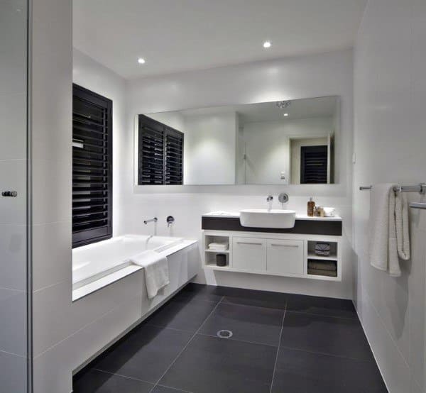 Modern bathroom with black floor tiles, white vanity, bathtub, and large mirror.