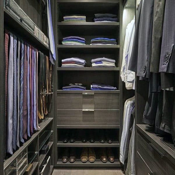 A neatly organized walk-in closet with folded clothes, hanging suits, ties, and shoes on shelves