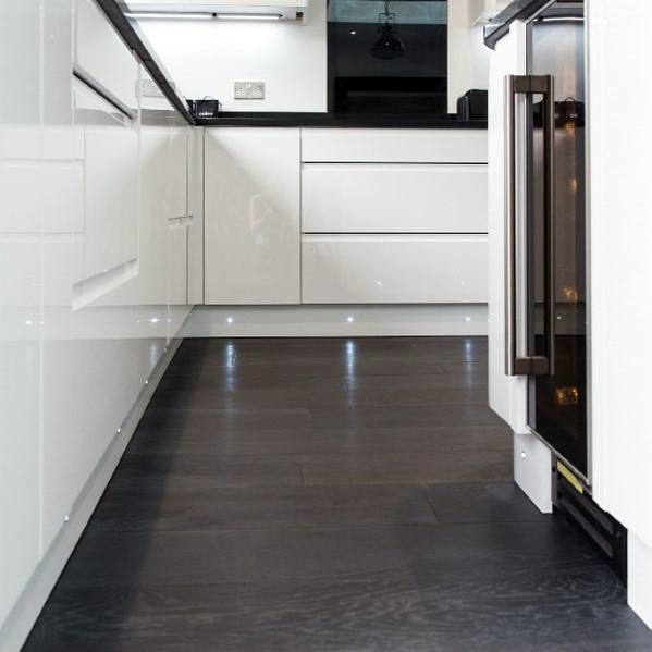 Sleek kitchen featuring dark hardwood flooring, glossy white cabinetry, and subtle under-cabinet lighting