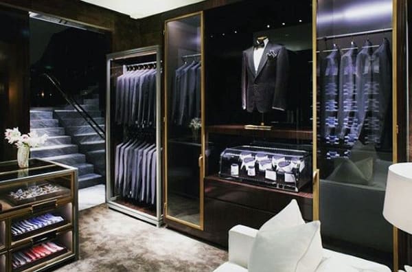 Luxurious walk-in closet with suits, dress shirts, ties, and a lit display case on dark wooden shelves