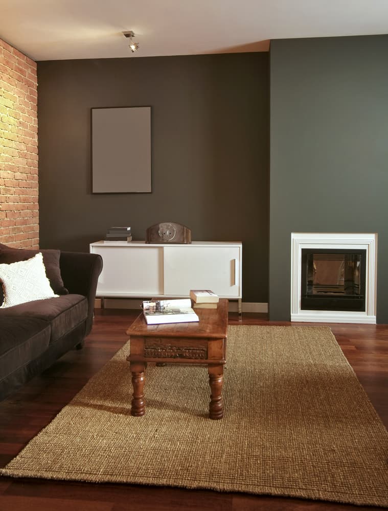 Cozy living room with a brown sofa, wooden coffee table, and brick accent wall beside a modern fireplace