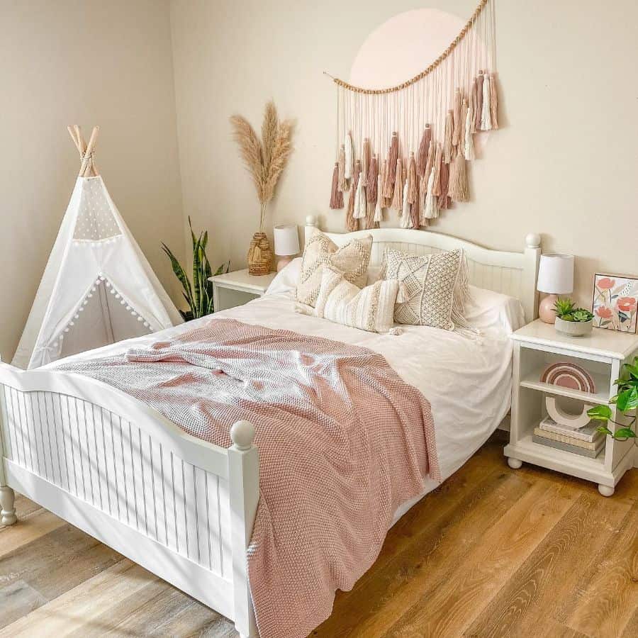 Boho bedroom with tassel wall hanging, teepee decor, pink bedding, and natural accents.