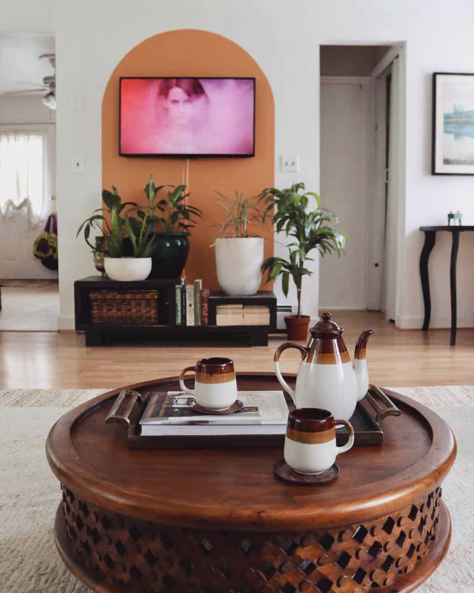 Cozy living room with a brown round table, tea set, plants, and TV on an orange accent wall