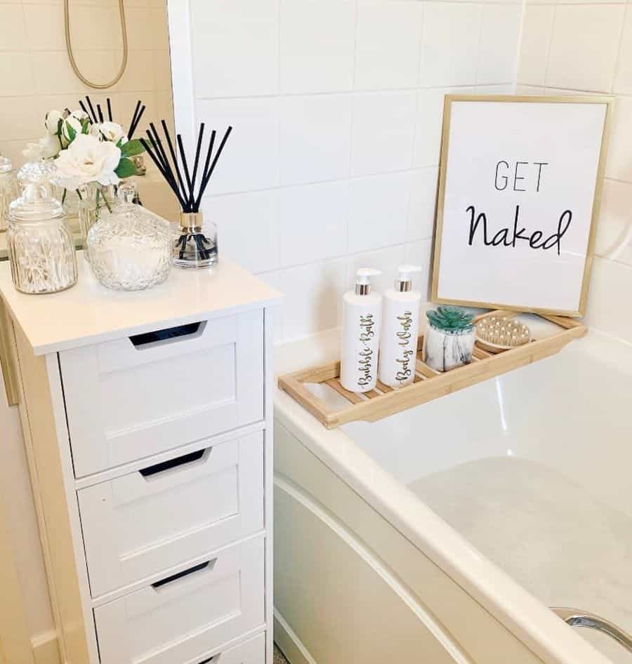 A bathroom with a tub, bath tray, bottles, candles, and a decorative sign saying "GET NAKED