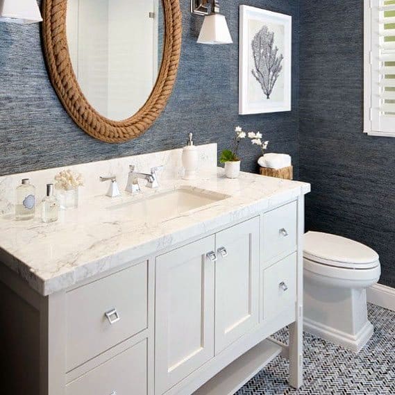 White toilet with marble vanity, blue textured walls, and rope-framed mirror.