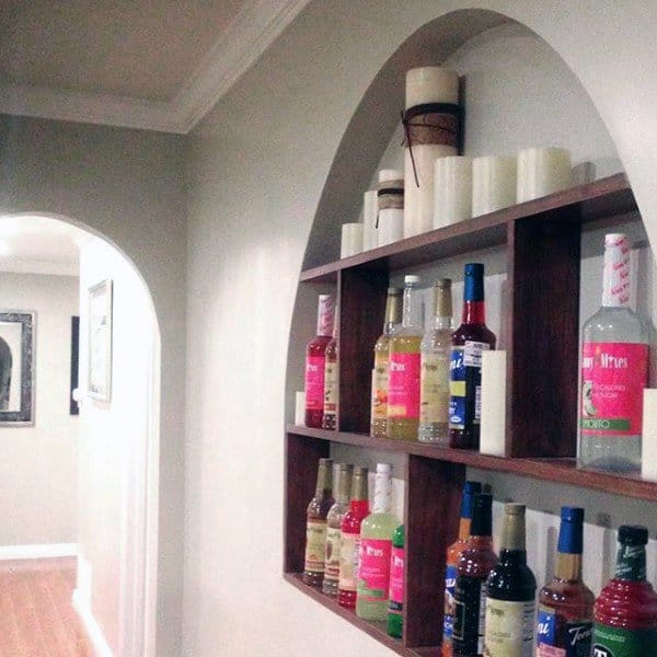 Wall-mounted mini bar with arched niche, wooden shelves, and colorful liquor bottle display.