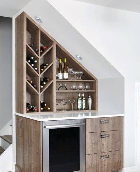 Under-stair mini bar with wood cabinets, wine rack, beverage fridge, and white countertop.