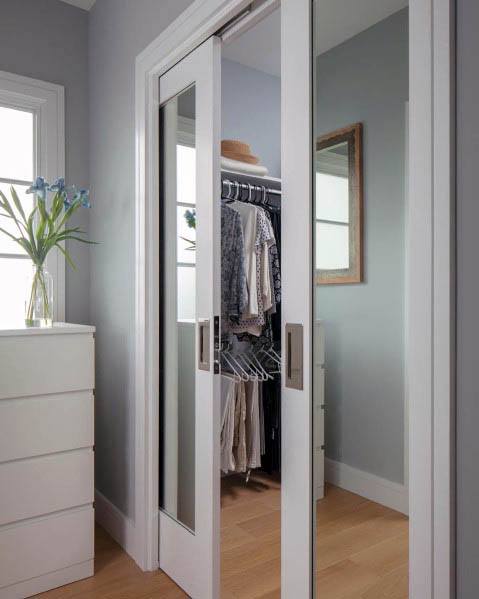 Modern mirrored pocket doors for a closet in a sleek bedroom with organized hanging clothes and light wood flooring