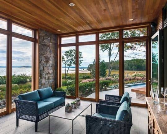 A sunroom with a wooden ceiling, stone accents, and blue wicker furniture.