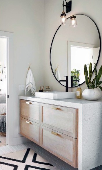 Modern bathroom vanity with light wood drawers, large round mirror, and black faucet.