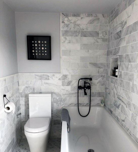 A sleek bathroom design featuring marble-patterned subway tiles, a white bathtub with black fixtures, and a matching modern toilet.