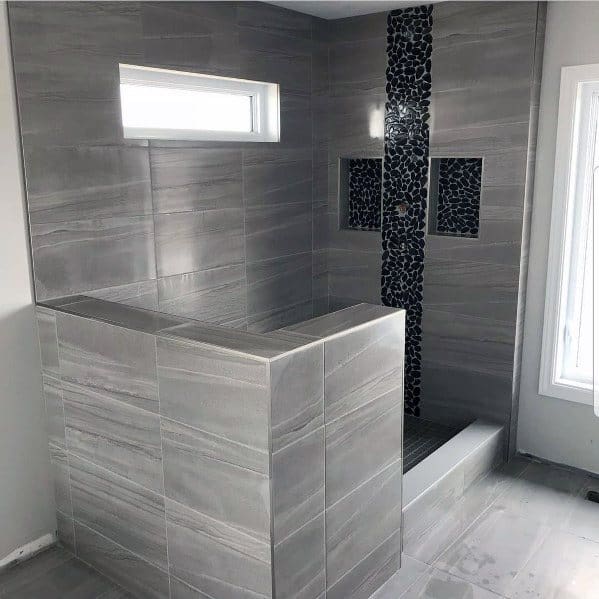 Modern shower with grey tiles, dark mosaic strip, small window, and built-in shelves