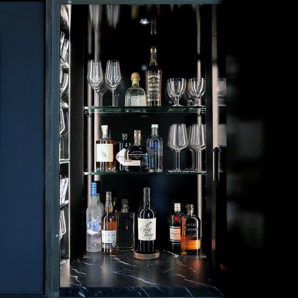 Modern mini bar with black marble countertop, glass shelves, and illuminated bottle display.