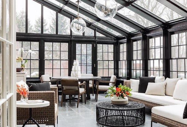 The sunroom features black-framed windows, rattan seating, and a modern dining area.