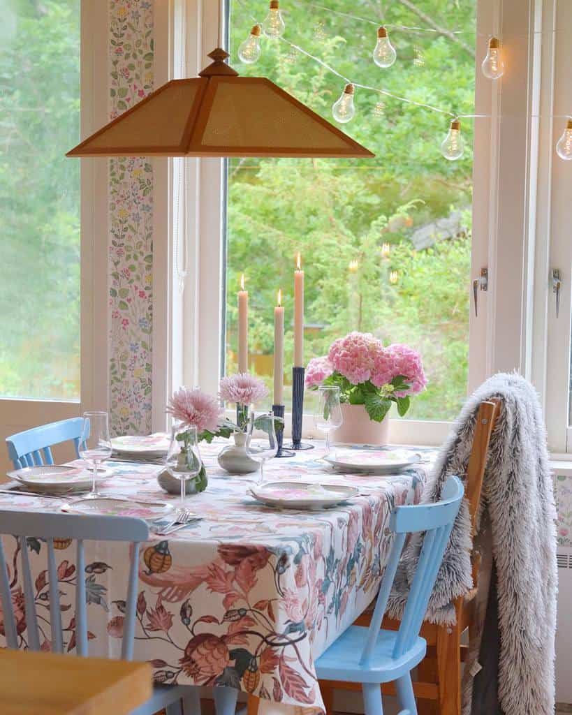 Charming dining sunroom with a floral tablecloth, pastel blue chairs, and soft candlelit ambiance.