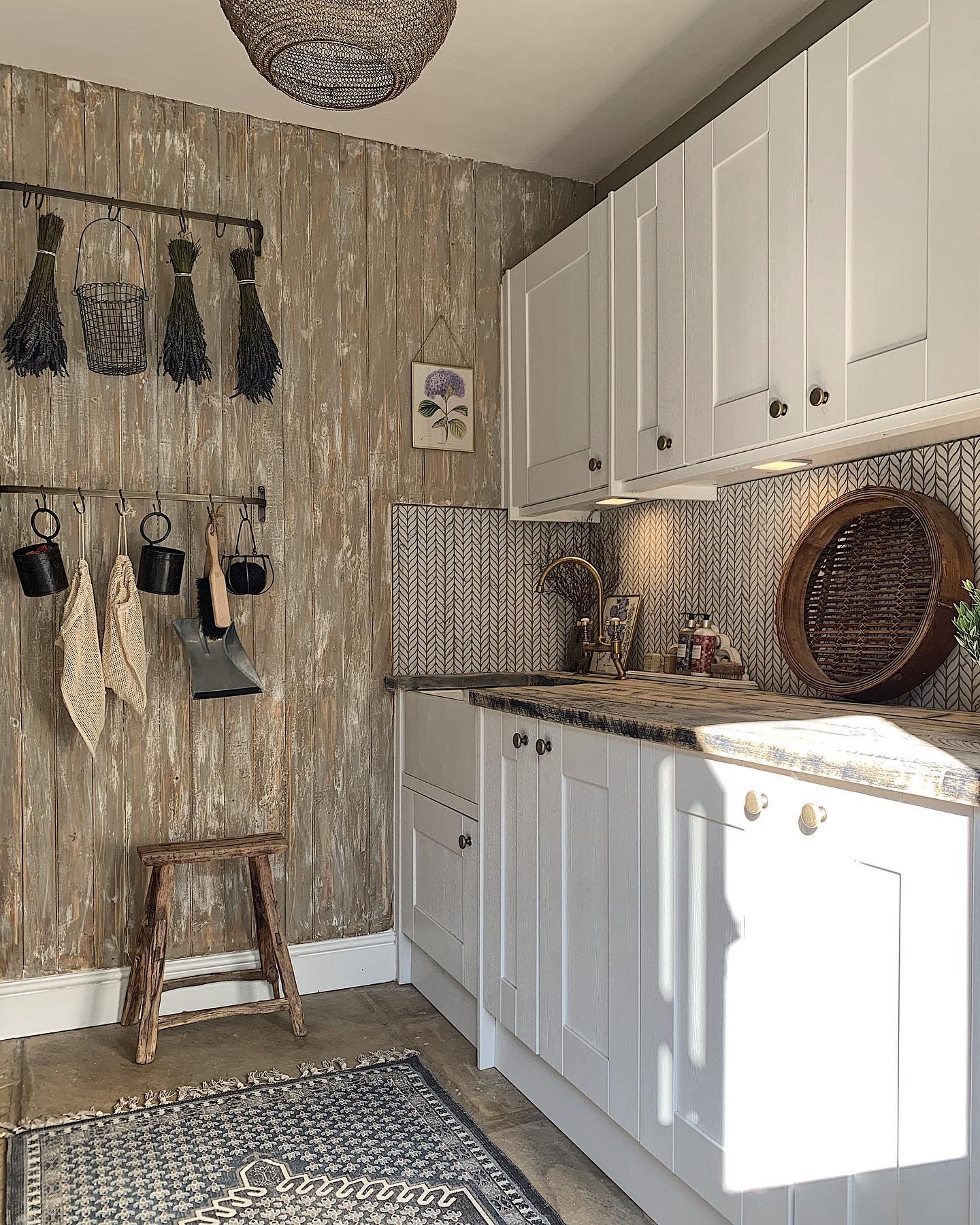 Cottage-style kitchen with white cabinets, rustic wood wall, and hanging decor elements.