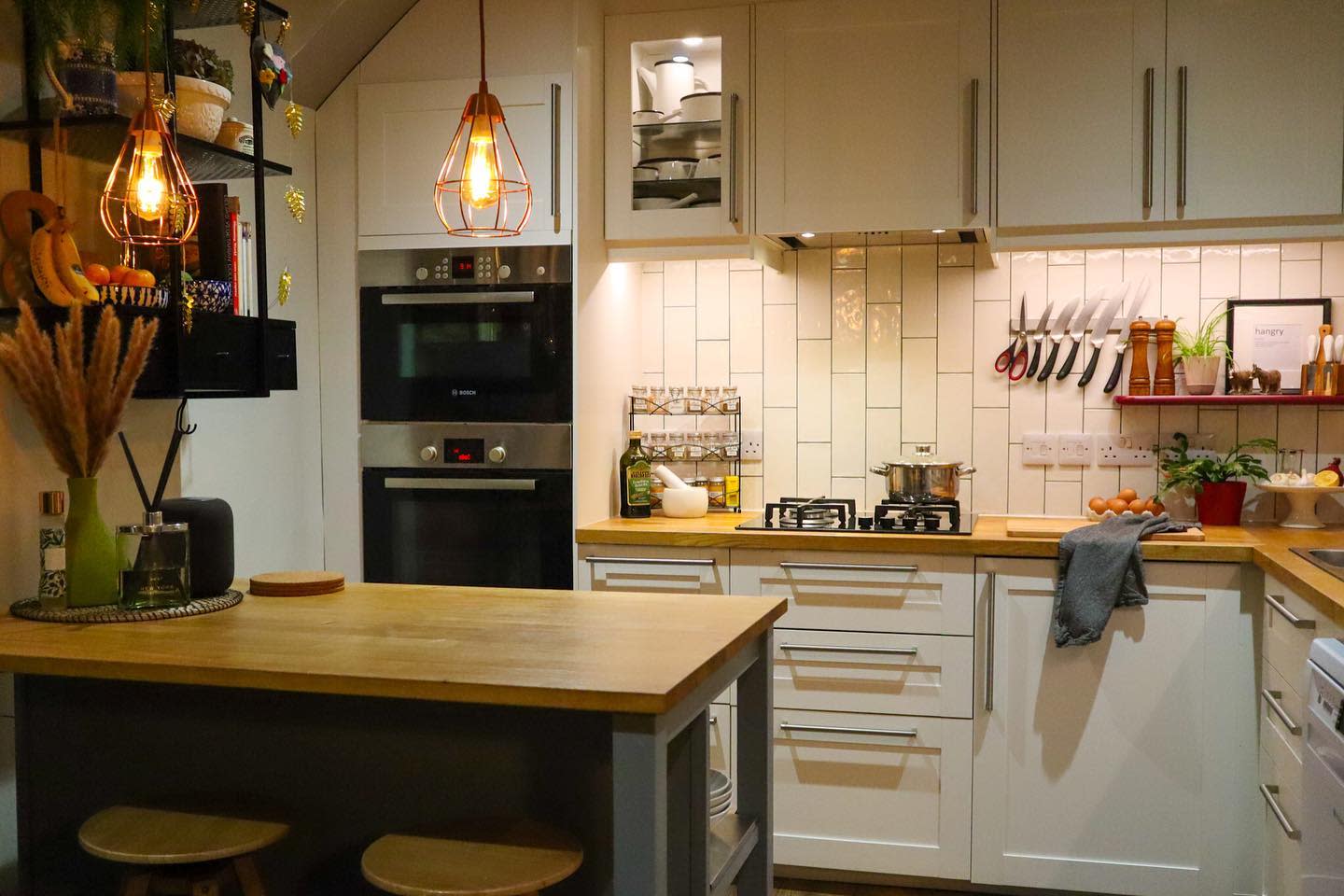 ountry-style modern kitchen with wood countertops, hanging lights, and white cabinets.