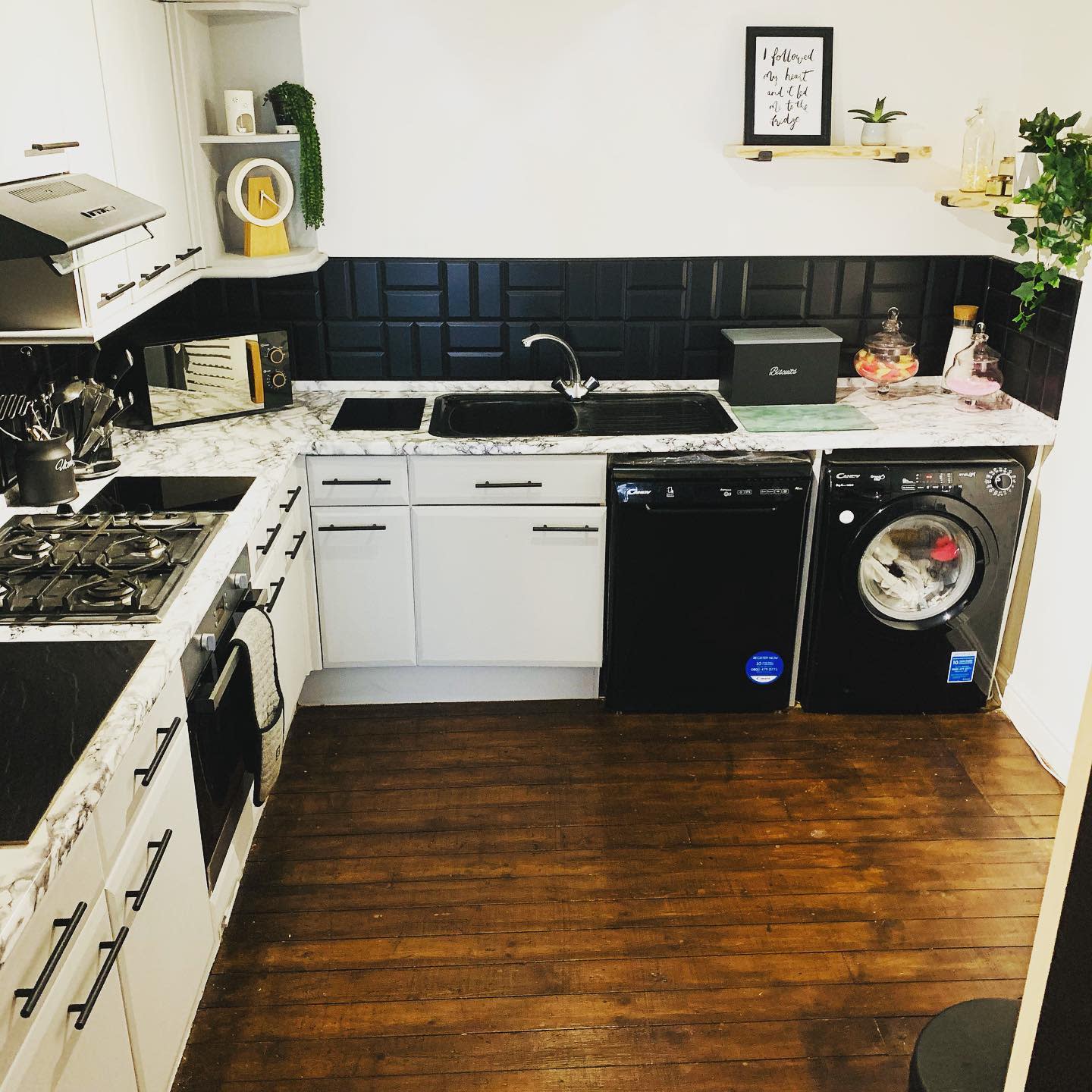 DIY basement kitchen with marble countertops, black tile backsplash, and built-in washing machine.