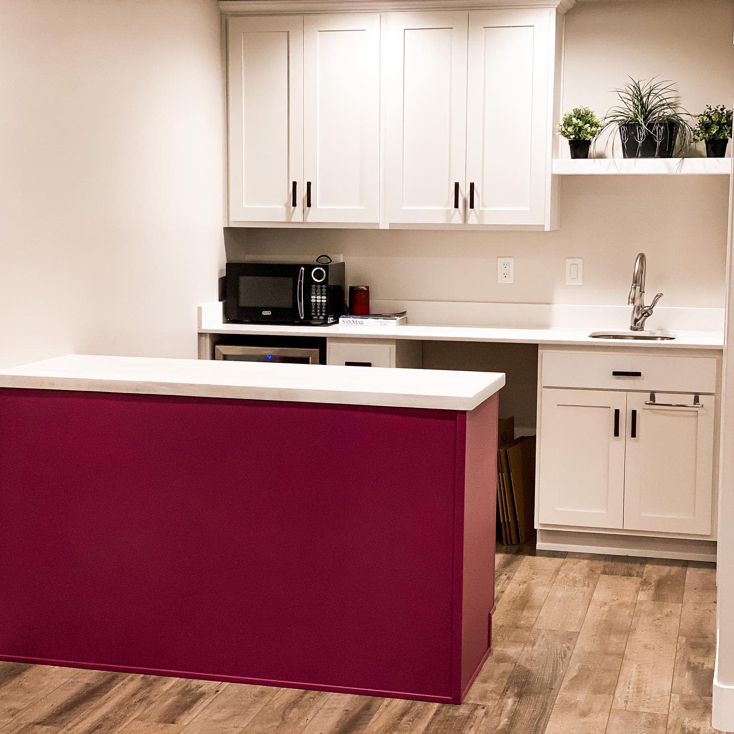 White kitchen with bold red island, wooden flooring, and sleek cabinetry.