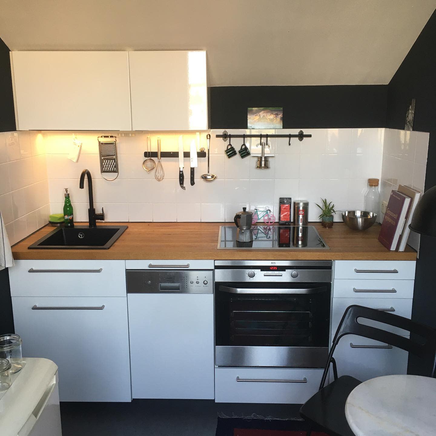 Modern white kitchen with wood benchtops, black sink, and under-cabinet lighting.