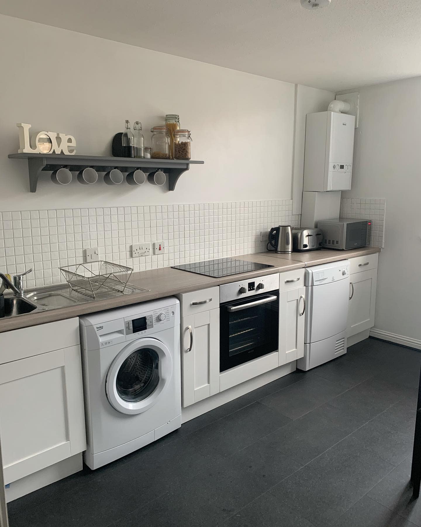 Modern white kitchen and laundry combo with open shelving and tiled backsplash.