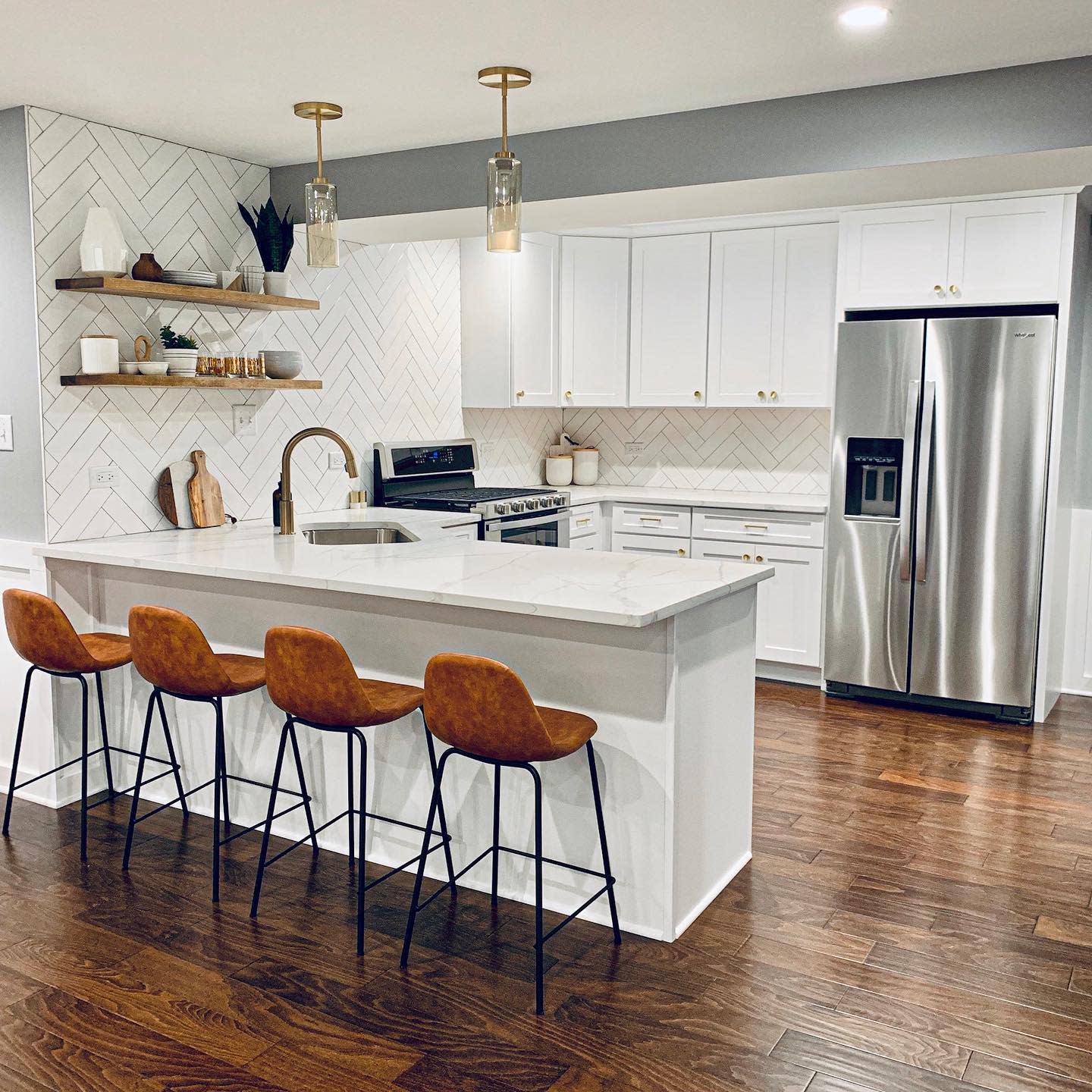 Modern white kitchen with herringbone tile, island seating, and dark wood floorboards.