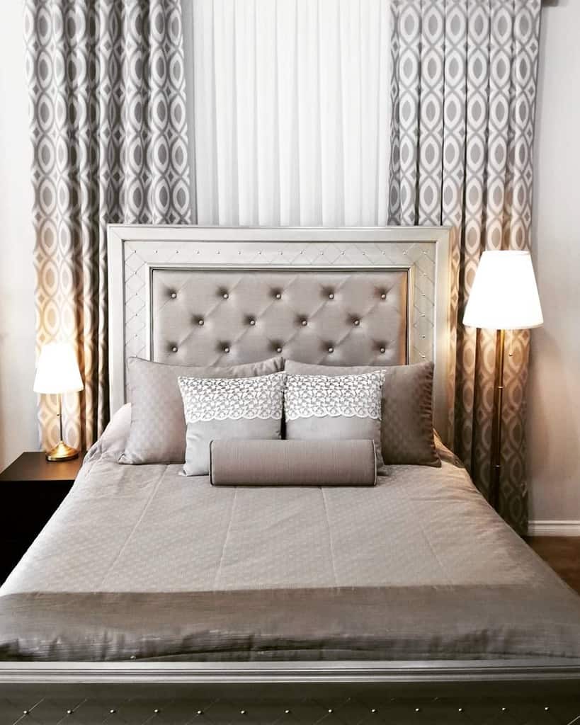 Elegant bedroom with tufted gray headboard, patterned curtains, and matching bedding.