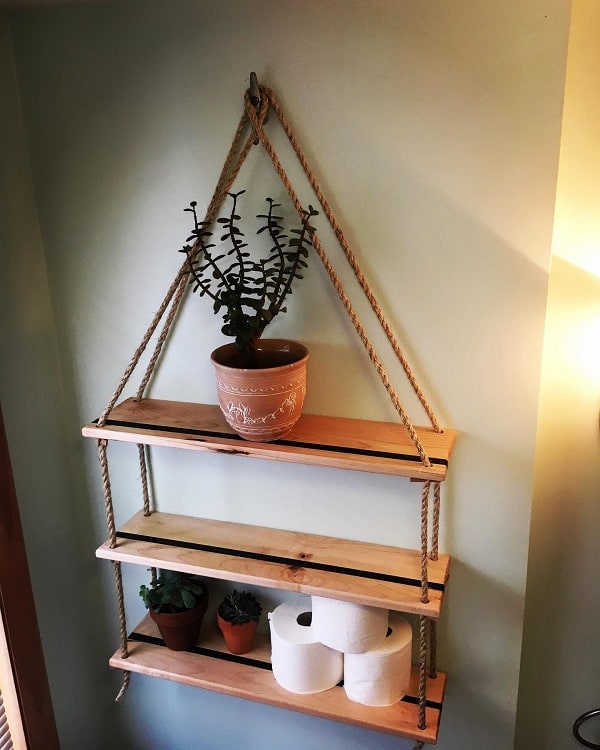 Hanging wooden bathroom shelf with potted plants and toilet paper rolls.