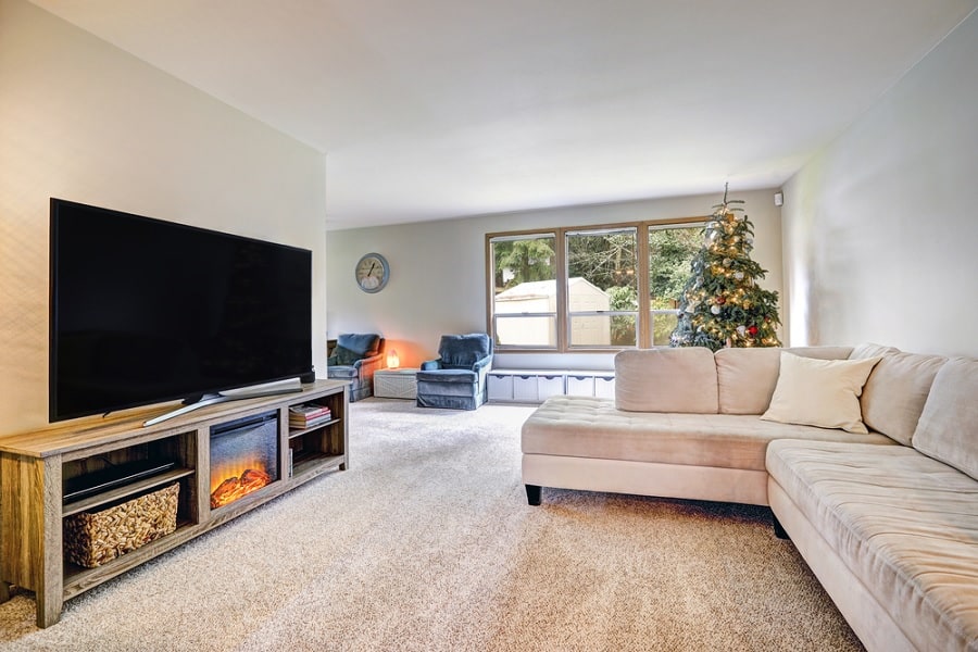 Electric fireplace in wooden TV stand with modern interior and beige sectional sofa.