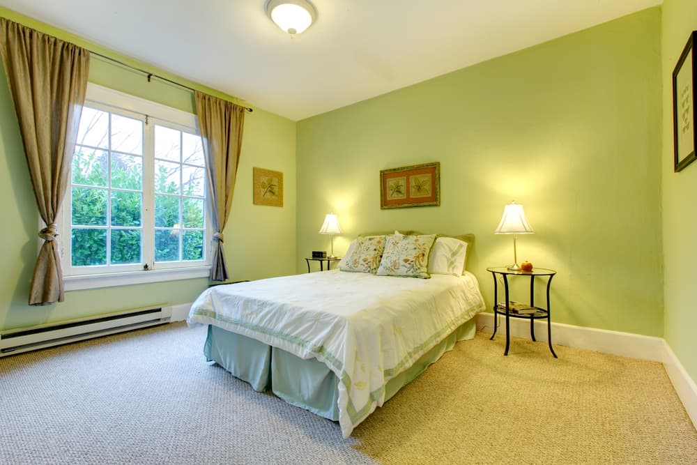 Cozy bedroom with green walls, a double bed, and lamps on side tables next to a large window with curtains