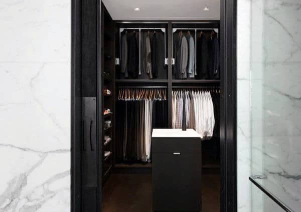 A neatly organized walk-in closet with hanging clothes and shelves, featuring a central drawer unit