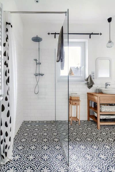 Bathroom with patterned tile floor, glass shower partition, white walls, and a wooden sink vanity under a window