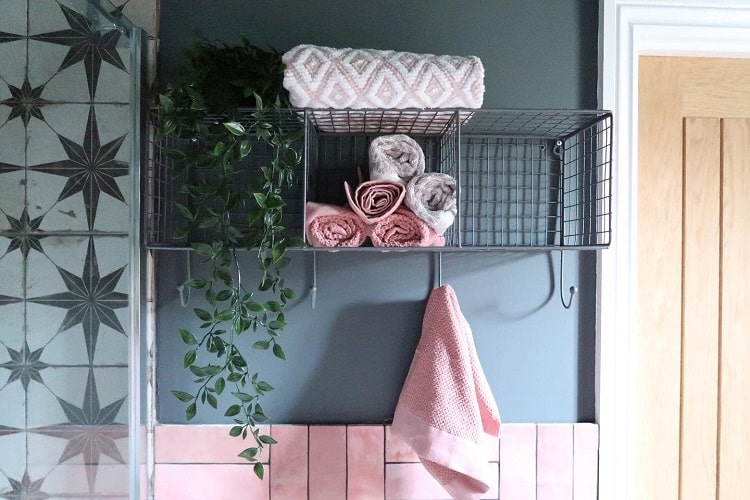 Metal bathroom shelves with rolled towels, hanging plant, and pink tile accents.