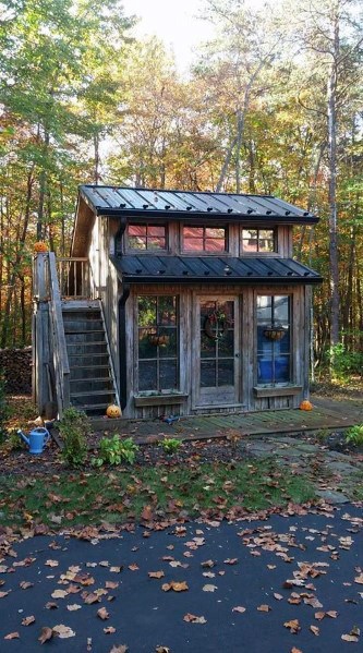 Two-story rustic wooden shed with large windows and outdoor stairs, surrounded by autumn trees.